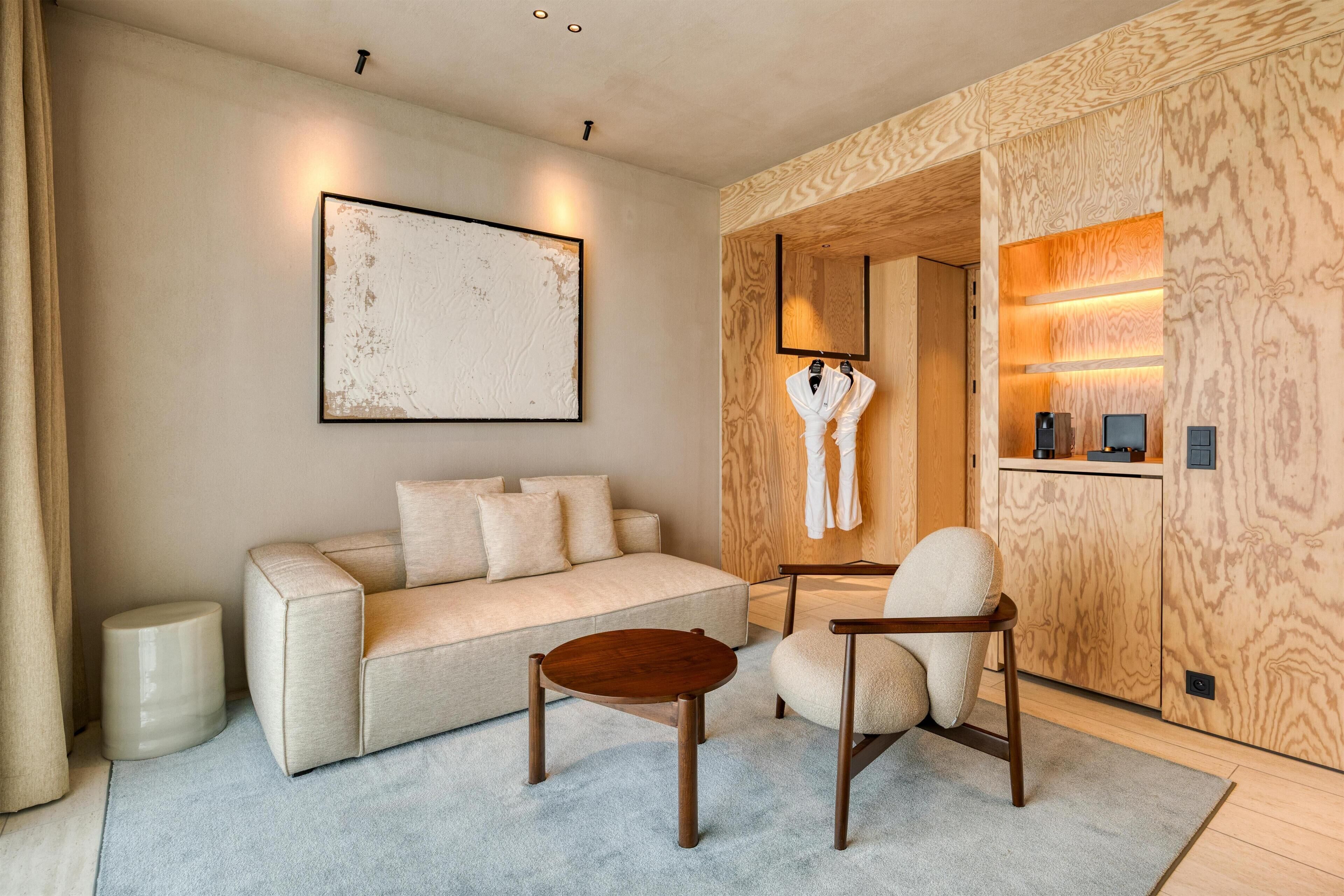 Een moderne woonkamer met een bank, fauteuil, salontafel en een kapstok met een badjas.