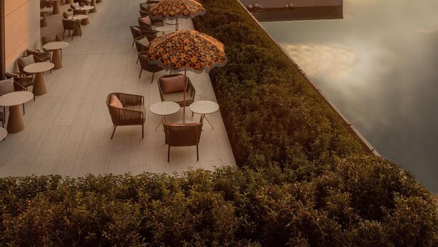 A modern building with a rooftop terrace featuring outdoor seating and umbrellas, overlooking a calm body of water and a sunset. - Radisson Collection The National Hotel, Brussels (Zaventem)