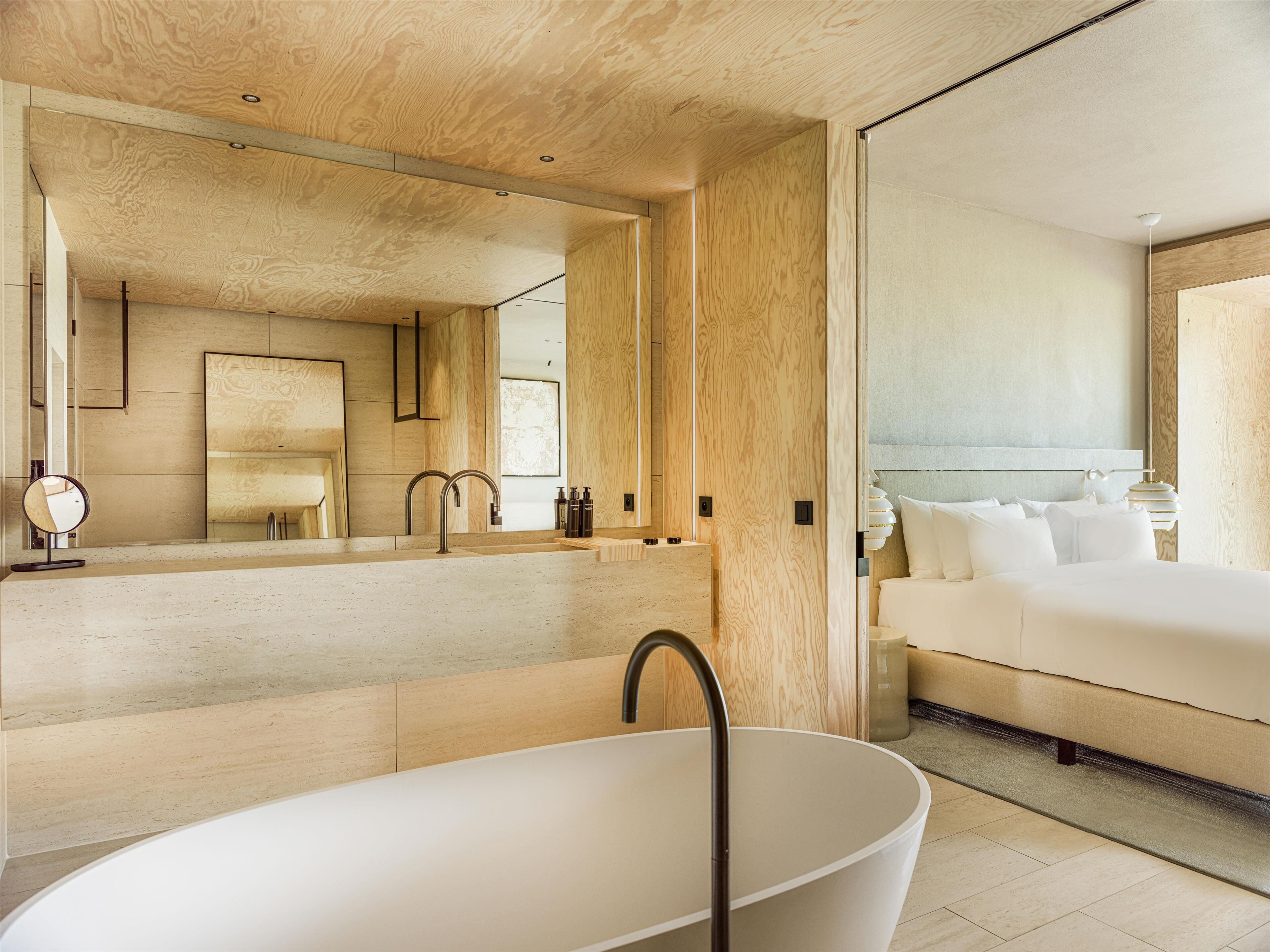 A modern bathroom with a freestanding bathtub, a large mirror, and a wooden ceiling.