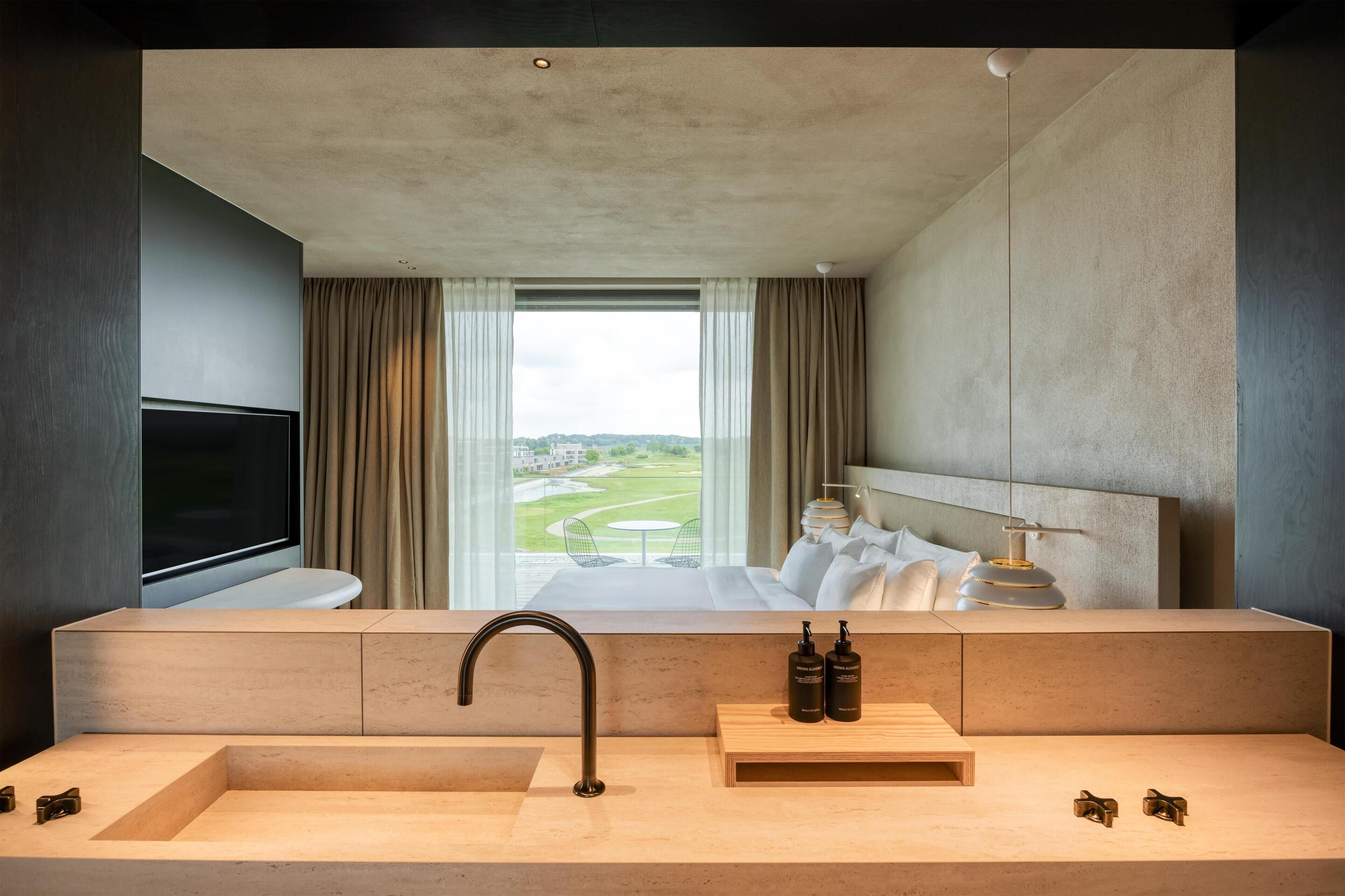 Une salle de bain d’hôtel moderne, dotée d’un grand lavabo, d’un miroir et offrant une vue sur une chambre d’hôtel avec un lit et un téléviseur.