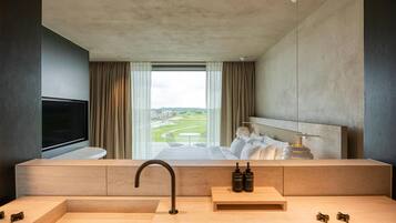 Une salle de bain d’hôtel moderne, dotée d’un grand lavabo, d’un miroir et offrant une vue sur une chambre d’hôtel avec un lit et un téléviseur.