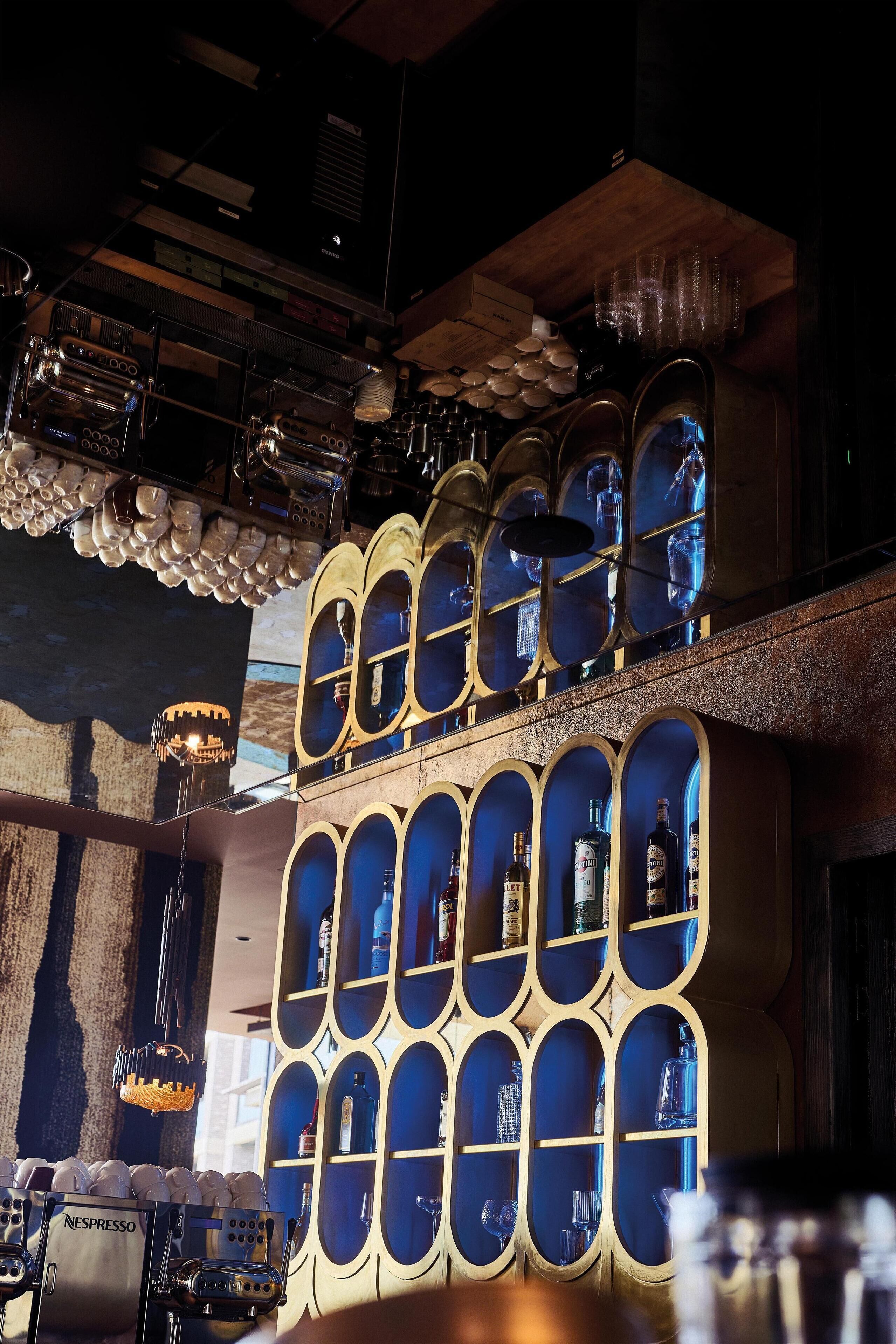 A bar area with a Nespresso machine, shelves with bottles, and a decorative ceiling with hanging lights.