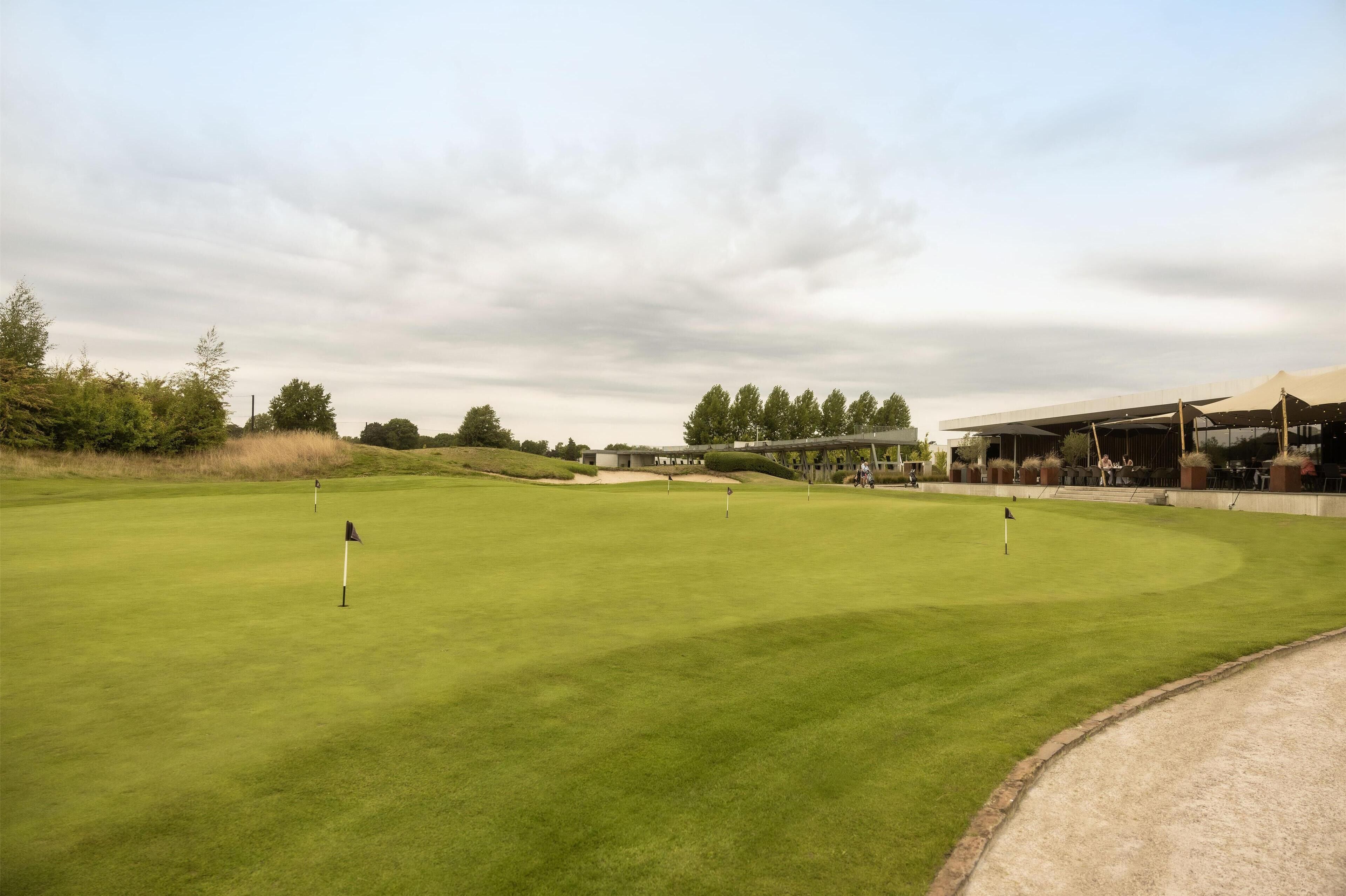 A golf course with a clubhouse, a putting green, and a sand bunker.