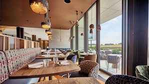 A modern restaurant with wooden tables and patterned seating, large windows offering a view of the outdoors. - Radisson Collection The National Hotel, Brussels (Zaventem)