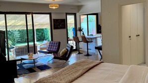 A spacious bedroom with a large bed, a seating area with chairs, and a view of the outdoors through large windows. - Studio with direct access to the sea and swimming pool in a green setting (Villeneuve-Loubet)