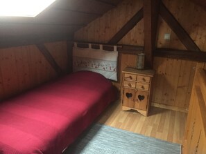 Une chambre à coucher avec un lit, une commode en bois ornée de découpes en forme de cœur et une fenêtre.