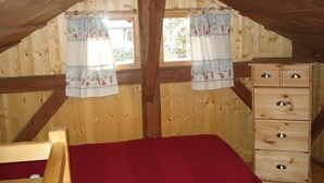 Een houten kamer met een bed, een dressoir en twee ramen met gordijnen.