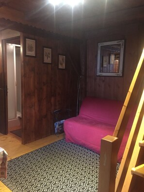 Une pièce aux murs en bois, un lit recouvert d’une couverture rose, un tapis à motifs et un tableau encadré accroché au mur.