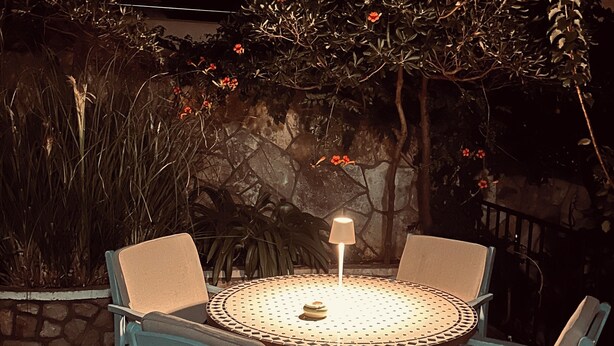 Una mesa redonda con cuatro sillas, una lámpara y una pared de piedra al fondo.