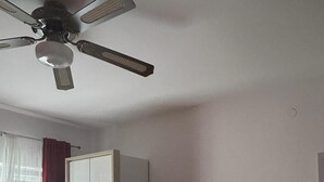 Un dormitorio con ventilador de techo, armario, televisor y cama.