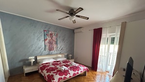Un dormitorio con cama, mesita de noche, ventilador de techo, ventana con cortinas y suelo de madera.