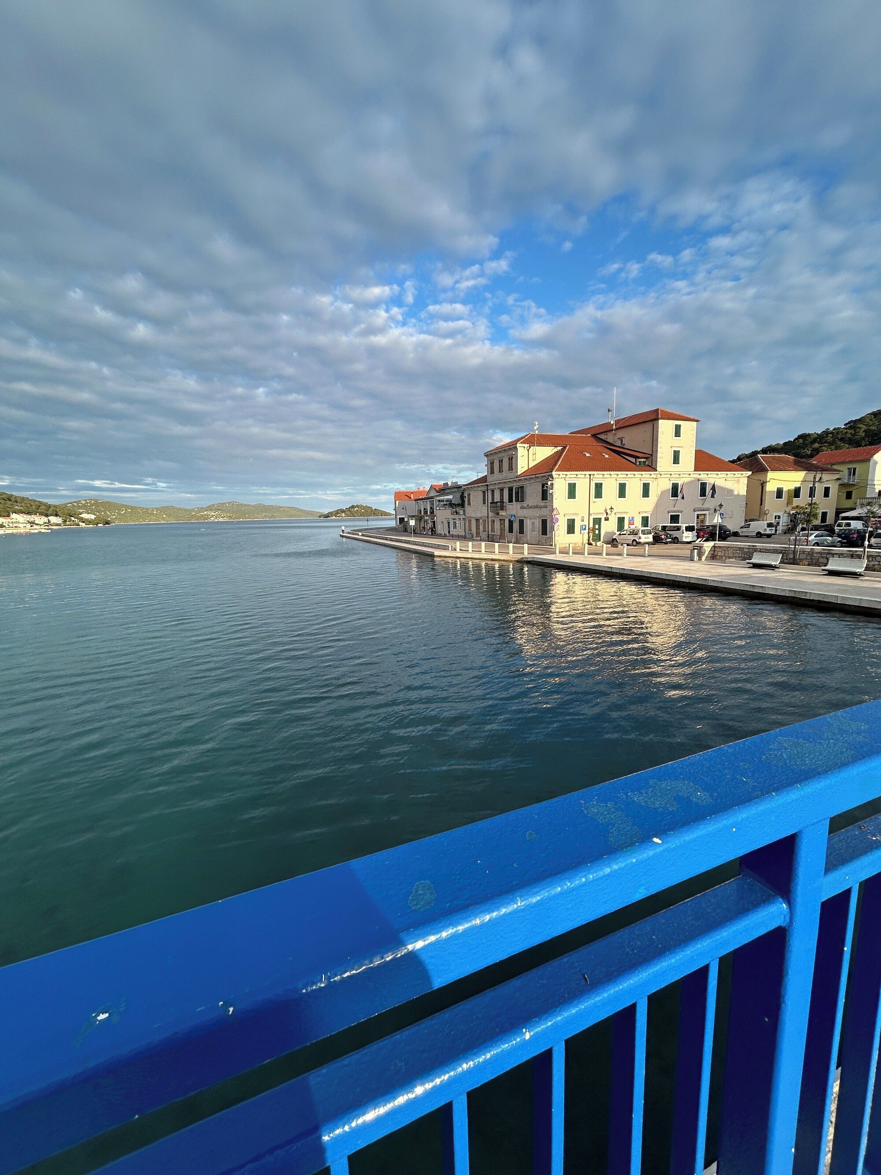Un bâtiment situé au bord de l’eau, avec un toit rouge, une jetée s’avançant dans une eau calme et un ciel dégagé.
