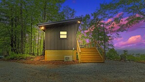 Une petite cabane avec un escalier en bois menant à une porte, le tout entouré d’arbres.
