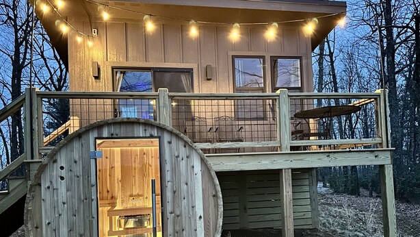 Une cabane en bois avec une porte ronde, une terrasse et des guirlandes lumineuses.