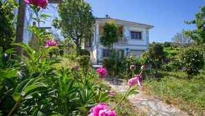 A two-story house with a stone pathway leading to the entrance, surrounded by lush greenery and flowering plants. - Villa with Private Pool, Mountain Views & Wi-Fi in Pantón, Ribeira Sacra (Pantón)