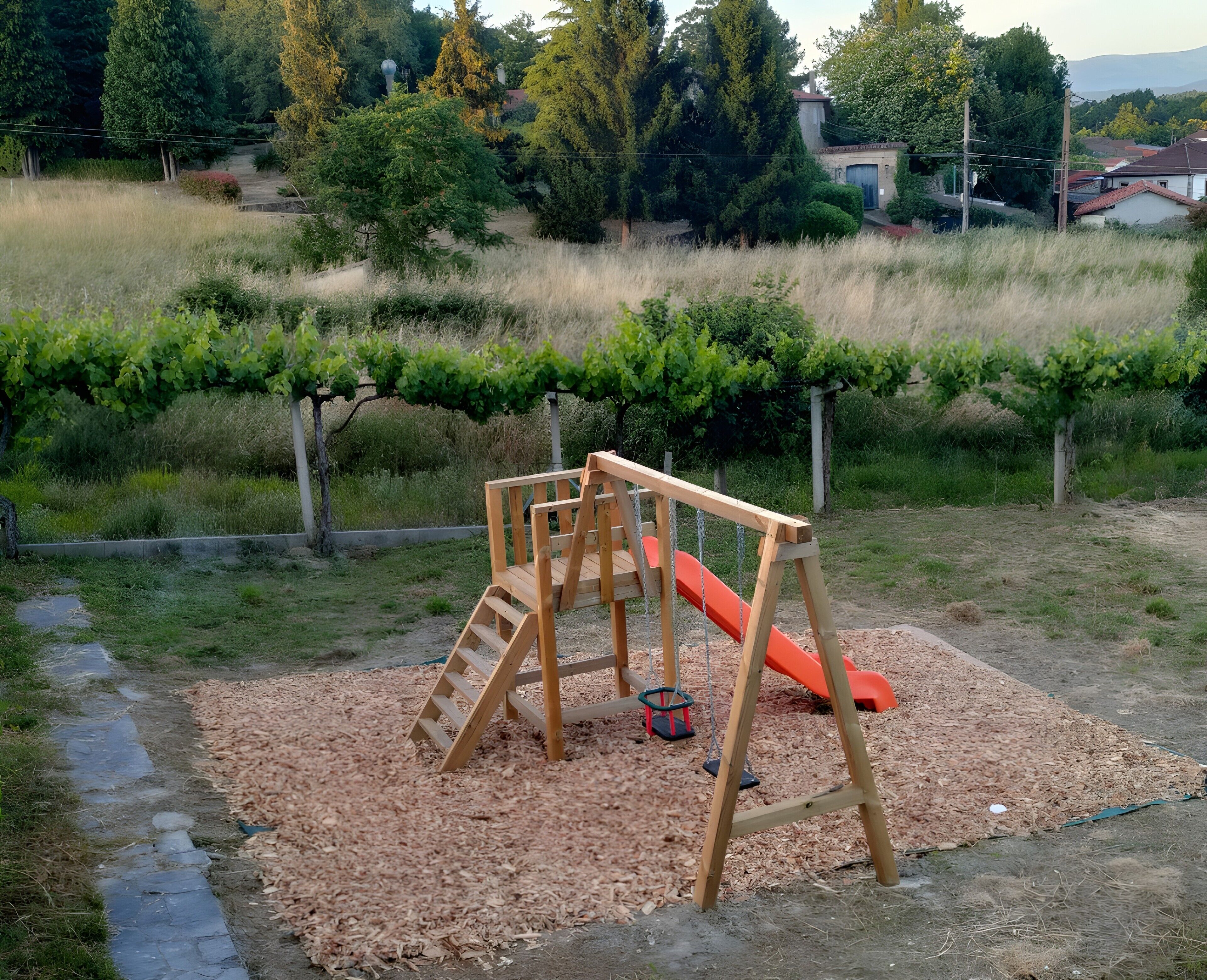 A playground with a wooden swing set and slide, surrounded by trees and a grassy area.