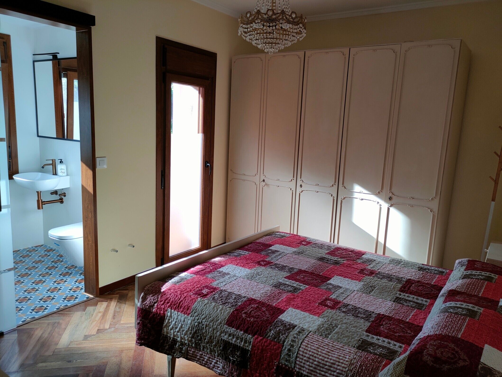 Un dormitorio con cama, armario, baño con lavabo e inodoro, y suelo estampado.