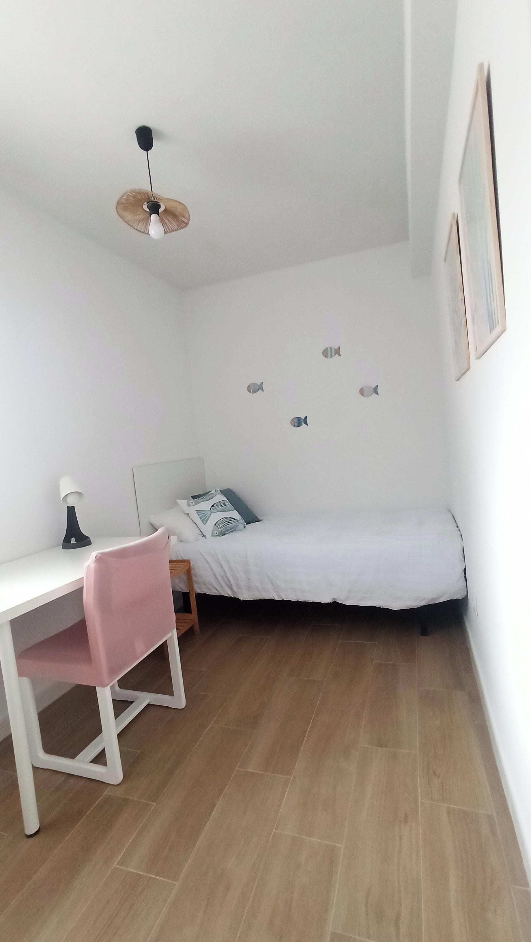 Una habitación pequeña y bien iluminada con una cama, un escritorio y una silla.