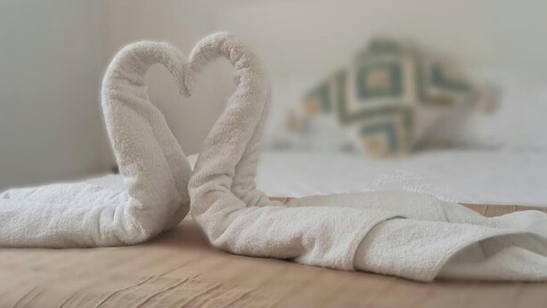 Ein Bett mit einer herzförmigen Handtuchanordnung und einer hängenden Dekoration darüber.