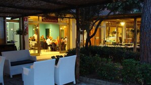 Un área de estar al aire libre con mobiliario de mimbre blanco y un restaurante al fondo.