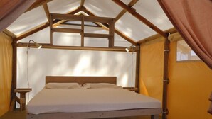 Una cama individual en una habitación tipo tienda con estructura de madera y colchón blanco.