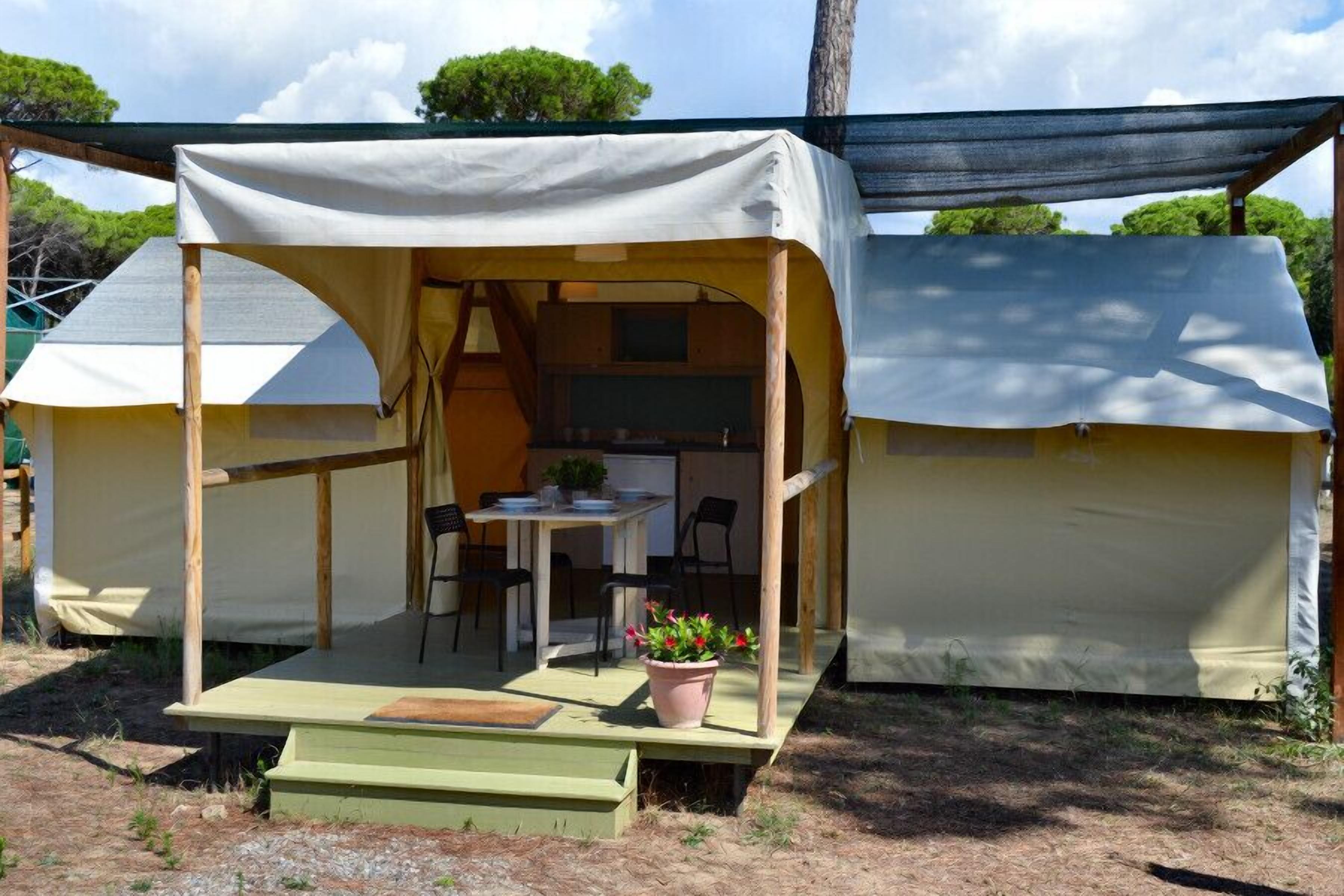 Un camping con dos tiendas de campaña, una con mesa y sillas, y una pequeña zona ajardinada.