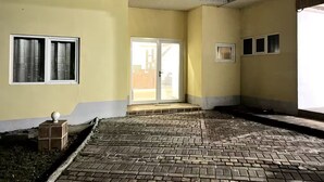 Un espacio al aire libre cubierto, con suelo de ladrillo, una puerta corrediza de vidrio y un ventanal.
