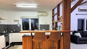 Una cocina moderna con una isla central, taburetes de bar y un sofá negro en una sala de estar.