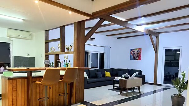 Amplia sala de estar con mostrador de cocina, taburetes de bar, sofá y mesa de centro.