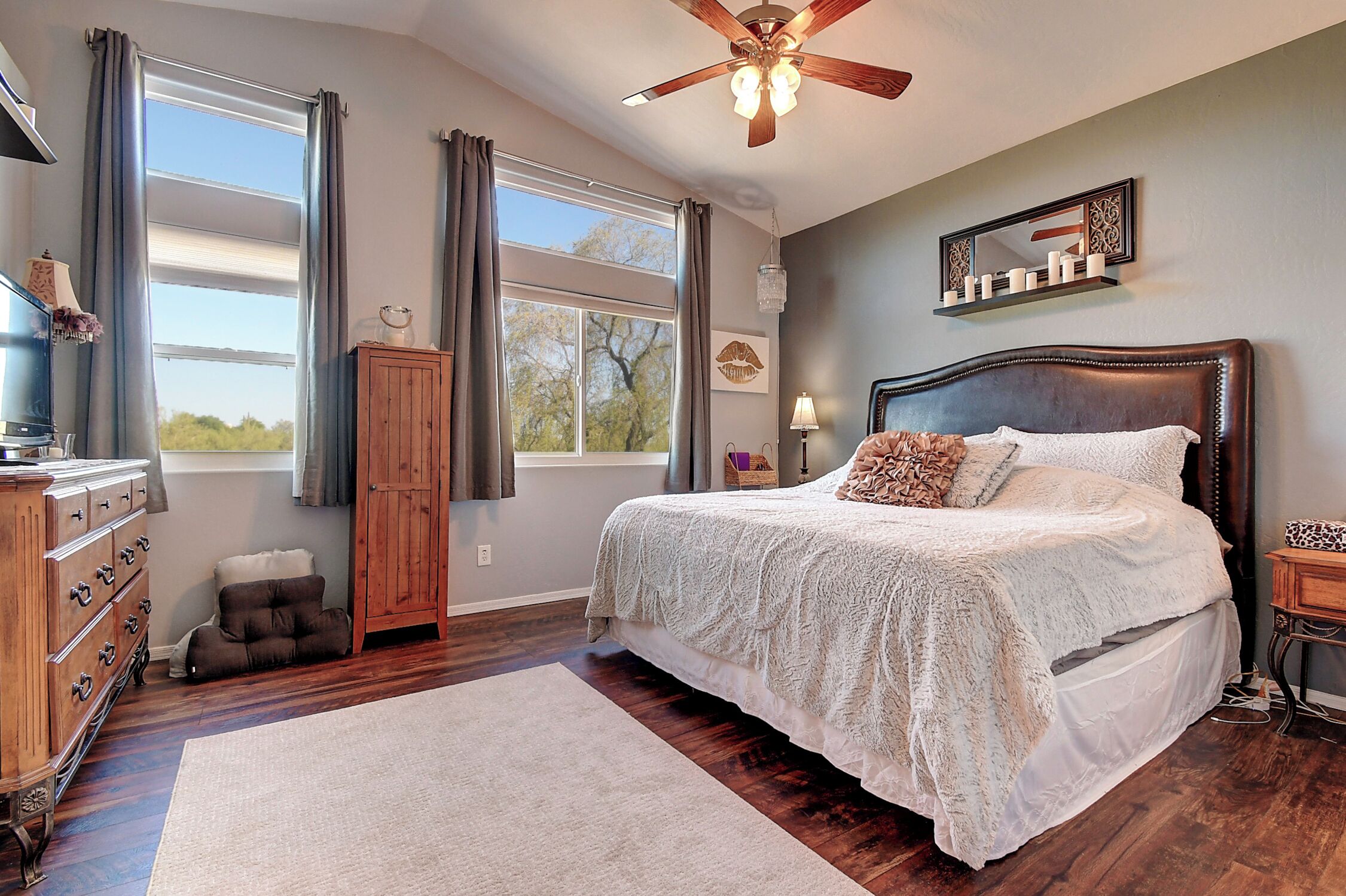 A bedroom with a large bed, wooden floor, and a ceiling fan.