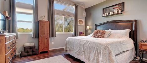 A bedroom with a large bed, wooden floor, and a ceiling fan.