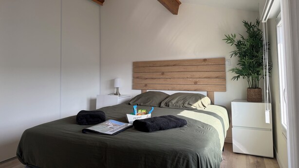 Un dormitorio con cama, mesita de noche, lámpara y una planta en maceta.
