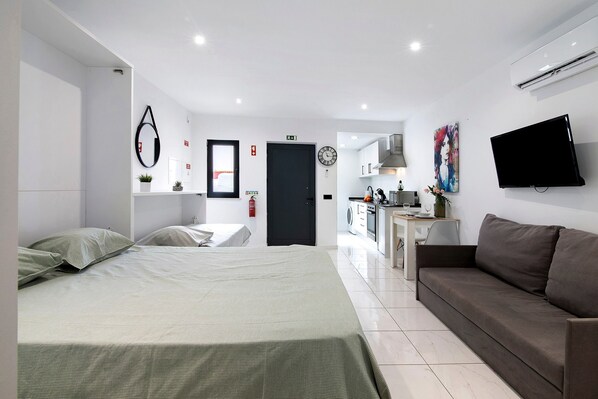 Une chambre d’hôtel moderne équipée d’un lit, d’un canapé, d’une télévision, d’un coin cuisine et d’une salle de bain.