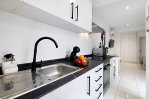 Une cuisine moderne dotée d’un évier en acier inoxydable, d’un robinet noir, de meubles blancs et d’un plan de travail noir.