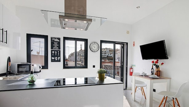 Eine moderne Küche mit Kochinsel, Essbereich mit Stühlen, einem Flachbildfernseher und Blick auf Gebäude durch große Fenster.