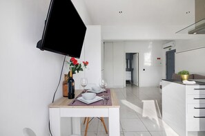 A modern kitchen with a dining area, a TV mounted on the wall, and a plant on the counter.