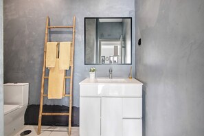 Ein Badezimmer mit einem weißen Waschbecken, einem Spiegel, einem Handtuch auf einer Holzleiter und einer Toilette.