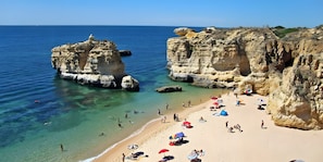 A beach with clear water, rocky cliffs, and people sunbathing.