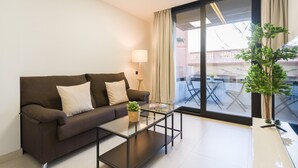 A modern living room with a sofa, a glass coffee table, and a view of an outdoor balcony. - Apartment in Las Palmas Near Las Canteras Beach (Las Palmas de Gran Canaria)