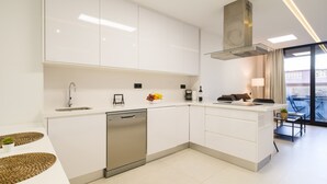 A modern kitchen with white cabinetry, a dishwasher, and a dining area with a glass table and chairs. - Apartment in Las Palmas Near Las Canteras Beach (Las Palmas de Gran Canaria)