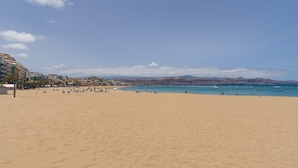 A wide sandy beach with a clear blue sky and distant mountains. - Apartment in Las Palmas Near Las Canteras Beach (Las Palmas de Gran Canaria)