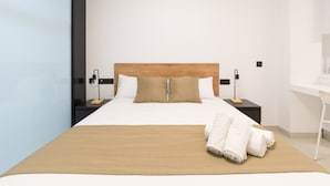 A modern hotel room with a large bed, wooden headboard, two bedside tables with lamps, a white desk, and a mirror. - Apartment in Las Palmas Near Las Canteras Beach (Las Palmas de Gran Canaria)