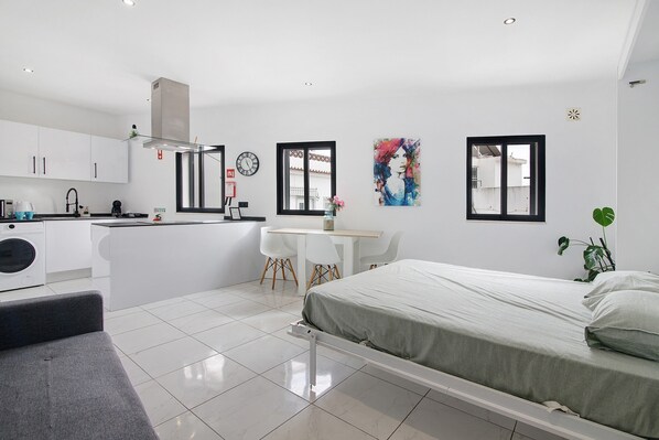 A modern bedroom with a bed, a desk, and a kitchenette.