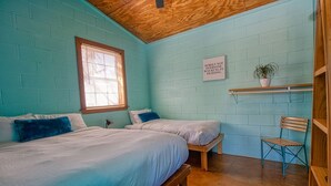 Een kamer met twee bedden, een raam, een plant op een plank en een stoel.