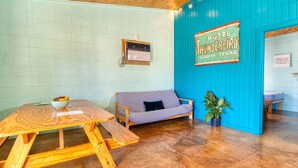 Een knus interieur met een houten tafel, een geruit bankje en een blauwe muur met een 'Motel Thunderbird' bord.