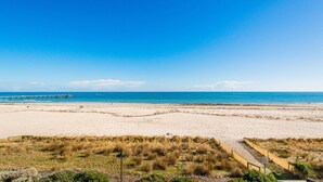 A beach with a pier extending into the sea, sandy dunes, and a clear sky.