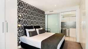 A modern hotel room with a large bed, a bathroom with a glass shower, and a kitchenette.