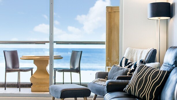 A balcony with a view of the sea, a sofa, two chairs, and a table.
