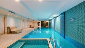 A modern indoor swimming pool with clear blue tiles, a wooden bench, and a 'No Diving' sign on the wall.
