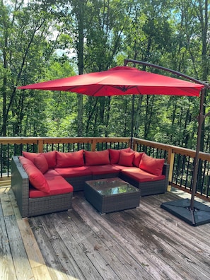 Une terrasse en bois avec un canapé d’angle rouge et une table basse en verre.
